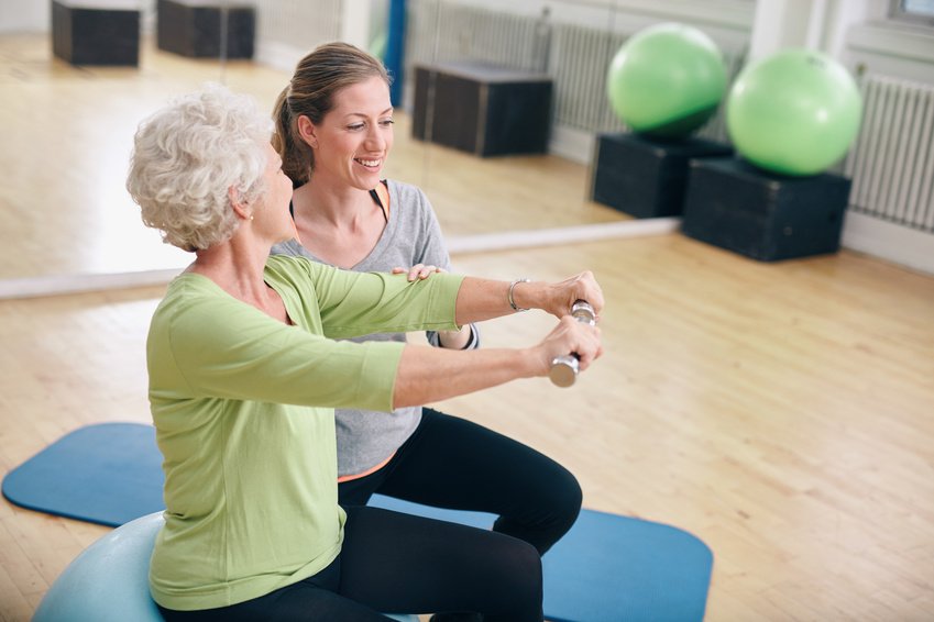 Senior woman assisted by personal trainer in gym